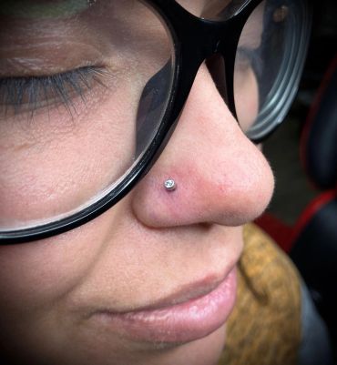 Close-up of a nose piercing with a small jewel and glasses.