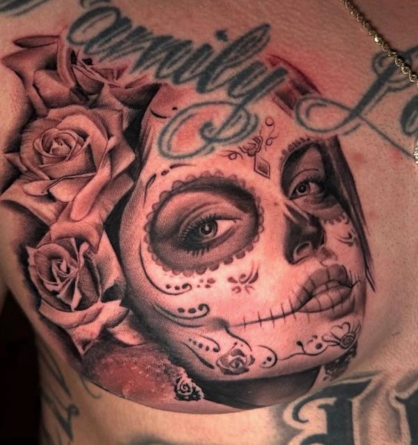 Intricate Day of the Dead sugar skull tattoo with roses and script on chest.