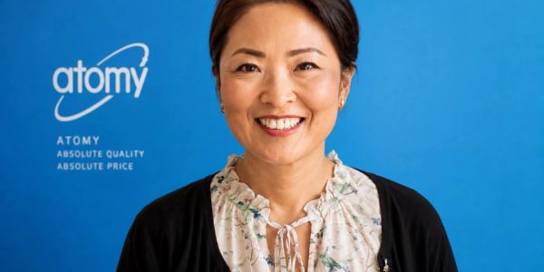 Smiling woman in front of a blue Atomy logo background.