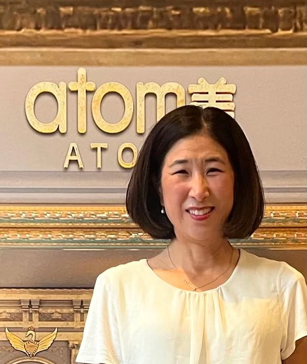 Smiling woman in front of a sign reading 'atomi'.