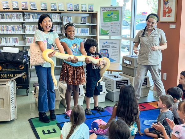 Three kids holding a snake at a library presentation.