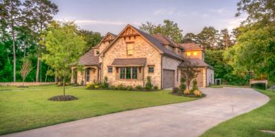 A stone-and-brick home with a curved driveway on a wooded lot at dusk in Johns Creek, Georgia.