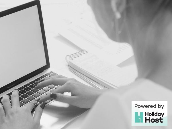 Person typing on a laptop with a notebook nearby in black and white.