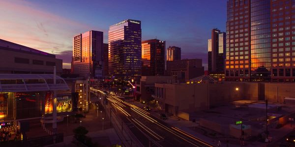 City skyline at dusk with illuminated buildings and light trails on the road.