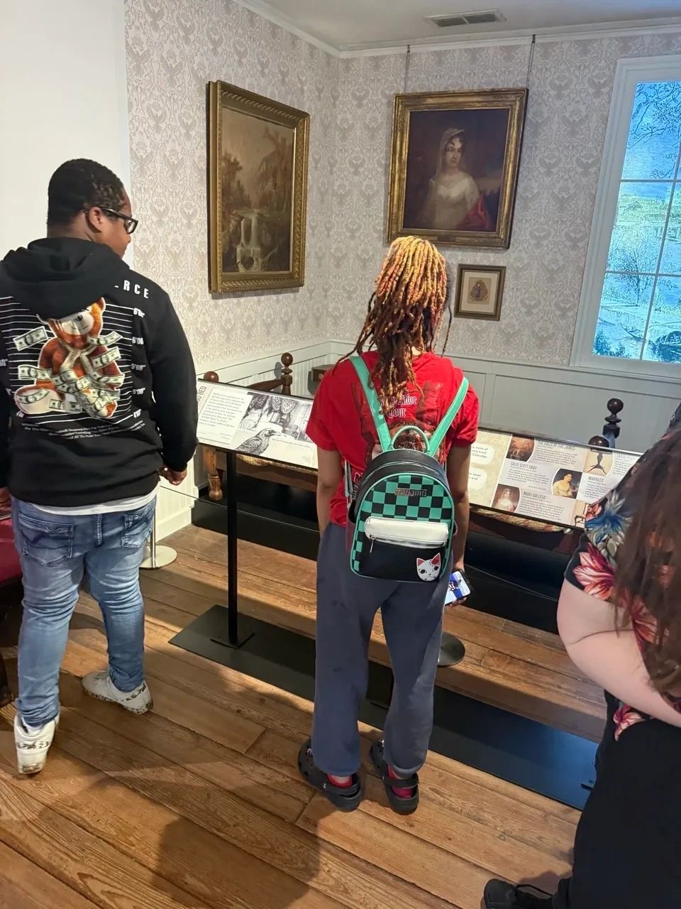Three people visiting a museum exhibit with paintings and display information.