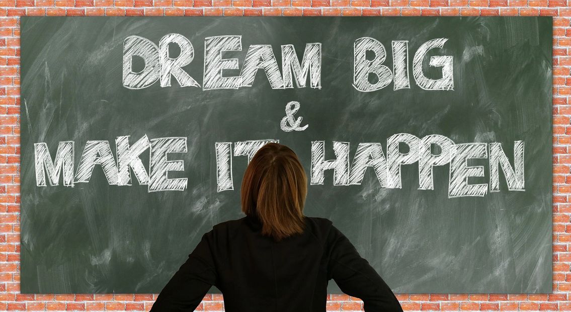 Woman standing in front of chalkboard that says Dream Big & Make it Happen