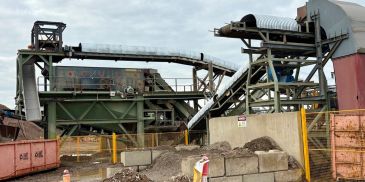Industrial site with conveyor belts and soil piles.