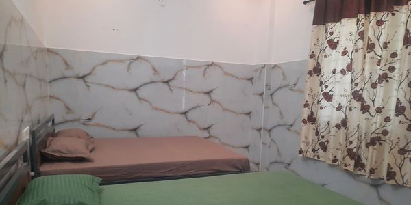 Two beds with green and brown bedding in a room with marble-patterned walls and floral curtains.