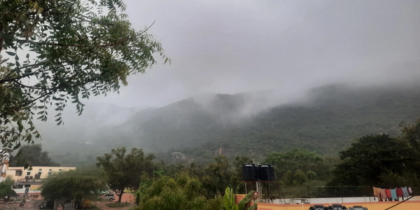 Foggy hills with lush greenery and water tanks on rooftops.