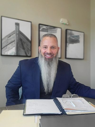 Man with a long beard smiling at a desk with papers and glasses.
