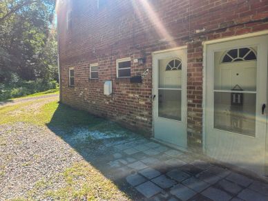 Sunlight on a brick building with two doors and a gravel path.