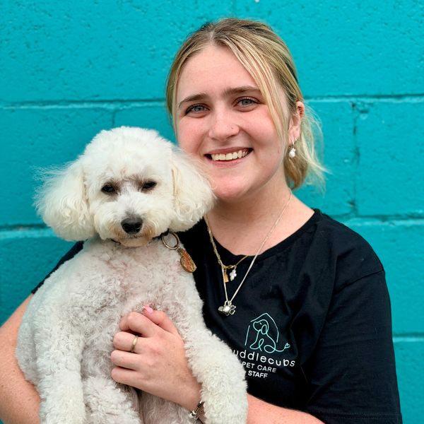 Woman smiling while holding a fluffy white dog against a turquoise wall.
