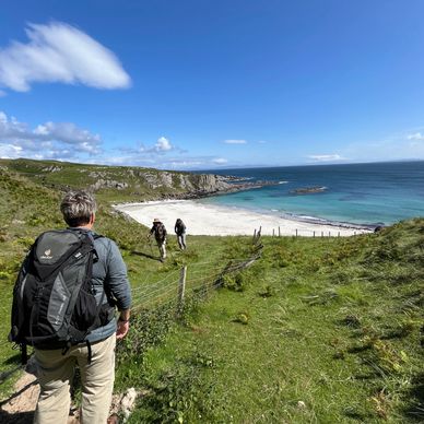 Hikers approaching a scenic beach on a sunny day with clear blue skies.