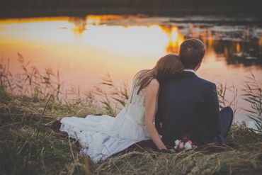 a bride and groom sitting at the waterside