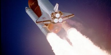 Space shuttle with boosters firing during liftoff against a dark sky.