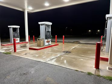 Empty gas station at night with wet pavement and red bollards.