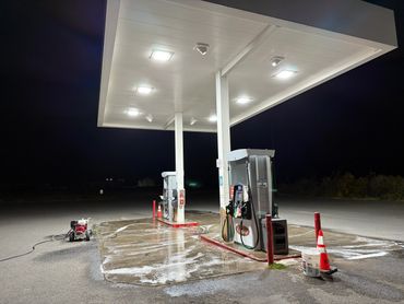 Gas station pumps being cleaned at night under bright lights.