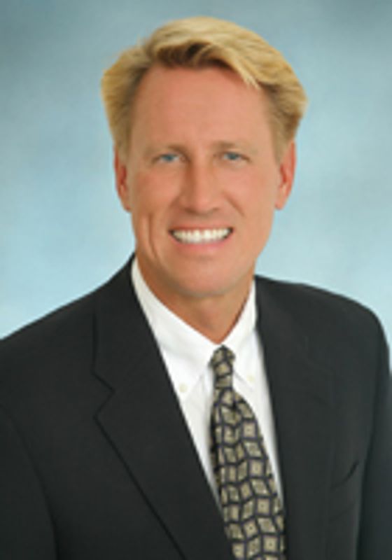 Smiling man in a suit and patterned tie against a blue background.