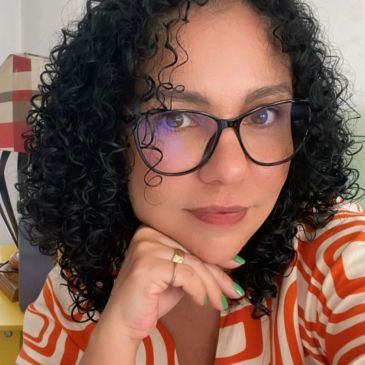 Woman with curly hair wearing glasses and an orange-striped shirt.