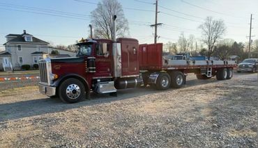 A large red semi-truck parked on a gravel lot near houses and power lines.