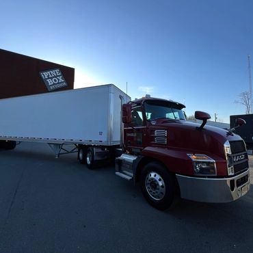 A red Mack semi-truck with a large white trailer parked near Pine Box Studios.