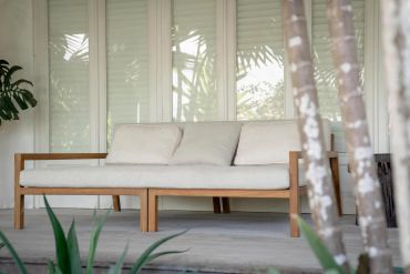 Modern wooden sofa with beige cushions on a porch surrounded by greenery.