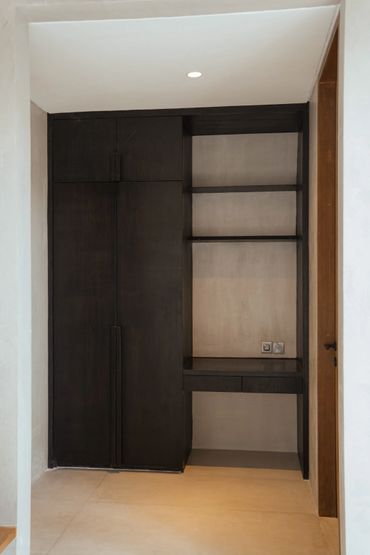 Minimalist black wooden cabinet with shelves and small drawers in a neutral-toned room.