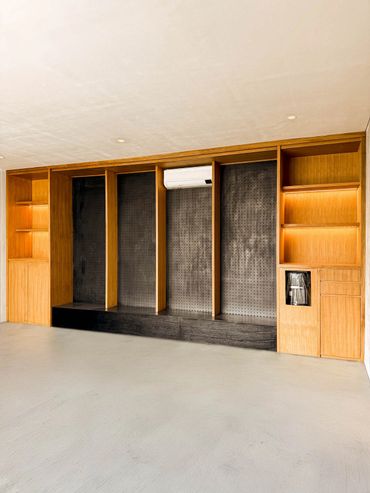 Minimalist modern wooden shelving unit with black pegboard and air conditioner.