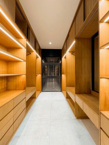 Modern wooden walk-in closet with built-in shelves and drawers.