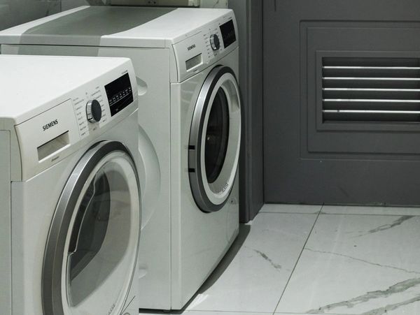 Two modern Siemens washing machines in a sleek laundry room with gray walls and marble flooring
