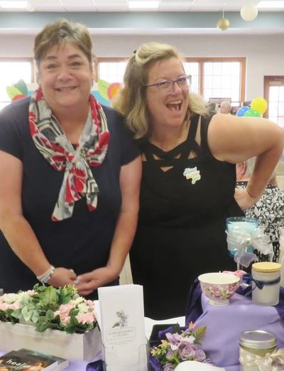 Two women smiling behind a decorated table with flowers and teacups.