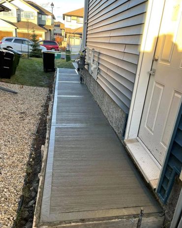 Freshly poured concrete walkway beside a house with siding and a door.
