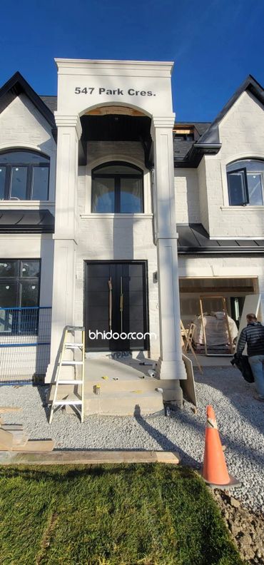 Modern house entrance under construction with black double doors and white stone facade.