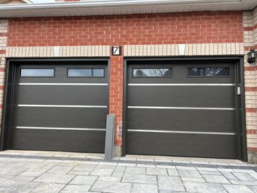 Two modern black garage doors with horizontal silver accents on a brick house.