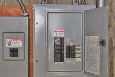 Open electrical panel with labeled circuit breakers and warning signs.