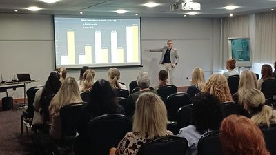 Andrew presenting to a room of delegates as he is stood in front of a bar chart on a big screen