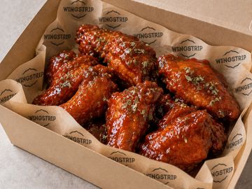 Box of glazed chicken wings sprinkled with herbs.