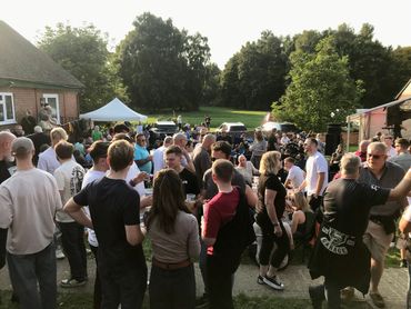 Large outdoor gathering with people socializing and enjoying drinks on a sunny day.