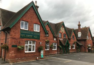 Brick village hall building with green trim and parking spaces.