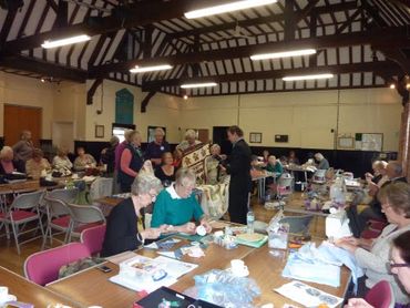 A group of elderly people engaged in quilting and sewing in a community hall.