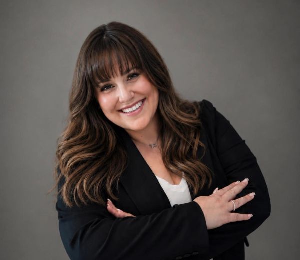 Smiling woman with long hair and bangs in a black blazer posing confidently.