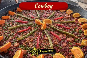 A large pan of cowboy paella garnished with asparagus, red peppers, peas, and orange slices.