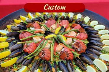 A vibrant custom seafood paella with lobster, shrimp, mussels, asparagus, and lemon wedges.