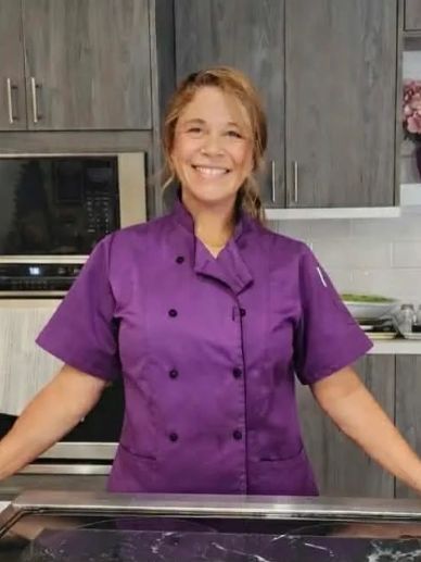 Smiling chef in a purple uniform in a modern kitchen.