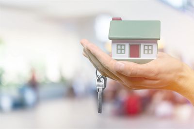Hand holding a model house with keys, symbolizing home ownership.