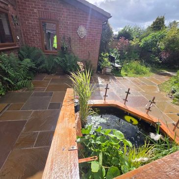 Sunlit garden pond and patio with lush greenery.