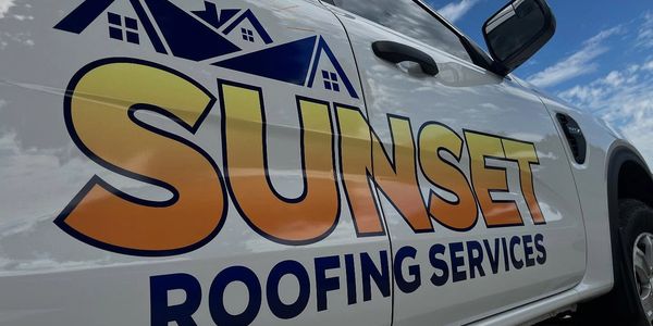 Close-up of a truck door with Sunset Roofing Services logo under a cloudy sky.