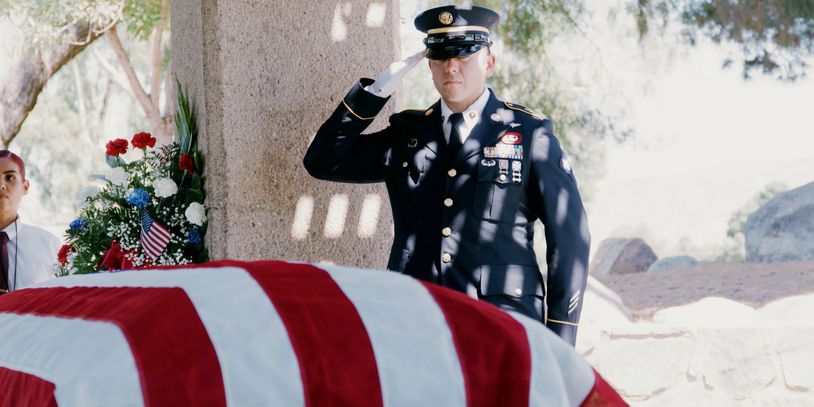 A military officer salutes a flag-draped coffin during a ceremony.