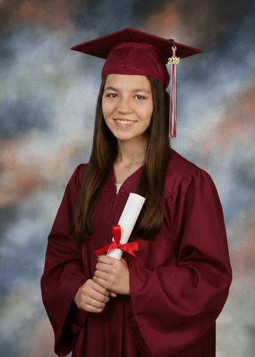 Young woman in maroon graduation gown holding diploma.
