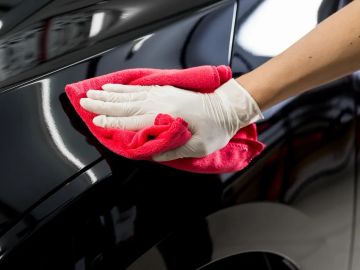 Person wearing gloves polishing a black car with a red cloth.